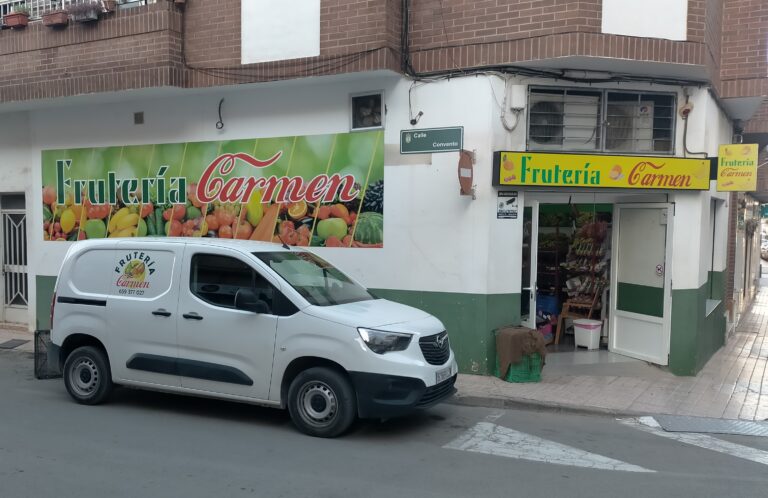 Furgoneta rotulada aparcada delante de una frutería con su rótulo de fachada